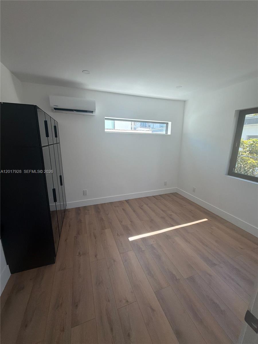 A bedroom features light wood-look flooring, white walls, a black wardrobe, and a mini-split unit — 7801 Byron Ave # 1, Miami Beach FL 33141, MIAMI BEACH, FL