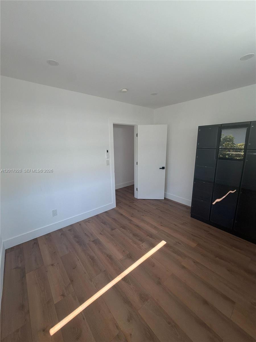 An empty room features white walls, wood-look flooring, a white door, and a black cabinet — 7801 Byron Ave # 1, Miami Beach FL 33141, MIAMI BEACH, FL