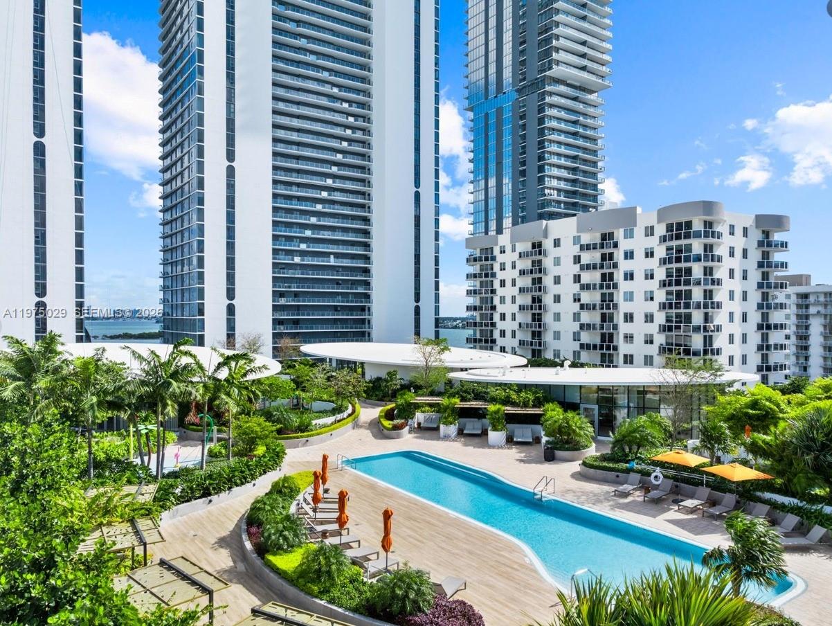 An outdoor swimming pool surrounded by lounge chairs, umbrellas, and landscaping between high-rise apartment buildings — 711 NE 23rd Ter # 1506, Miami FL 33137, MIAMI, FL