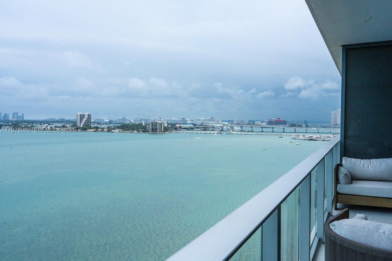 A balcony with outdoor seating overlooks a bay, a bridge, and a distant city skyline — 711 NE 23rd Ter # 1506, Miami FL 33137, MIAMI, FL