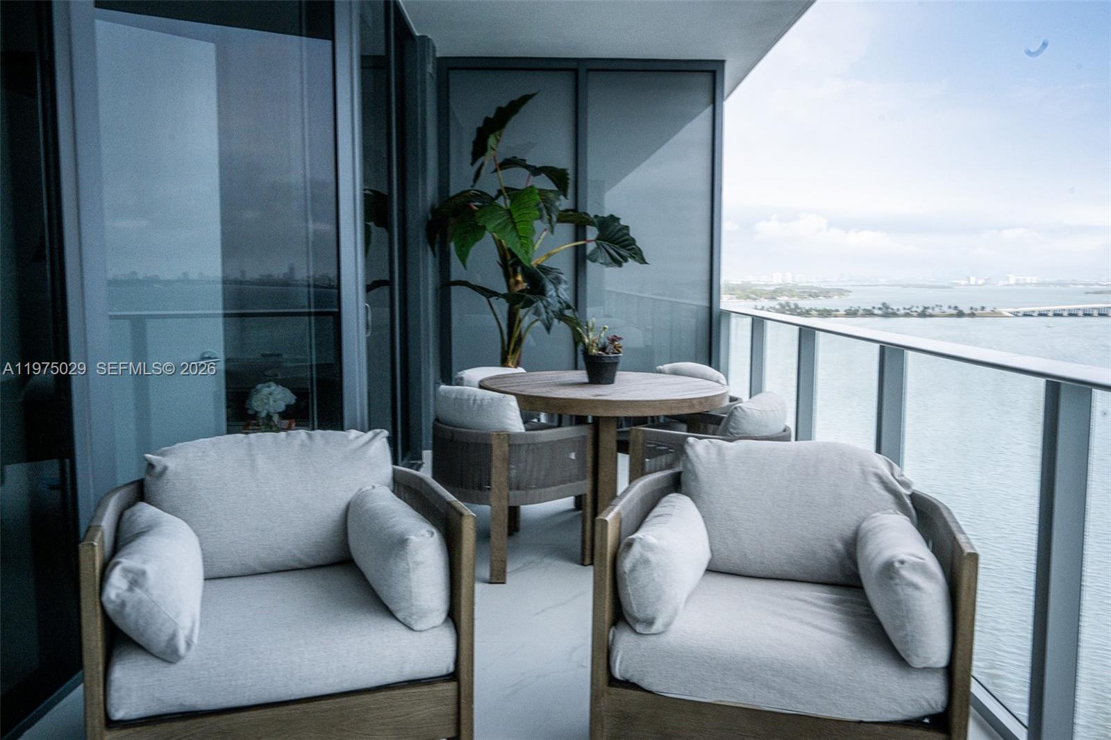 A balcony features two armchairs, a round dining table with chairs, and a water view — 711 NE 23rd Ter # 1506, Miami FL 33137, MIAMI, FL
