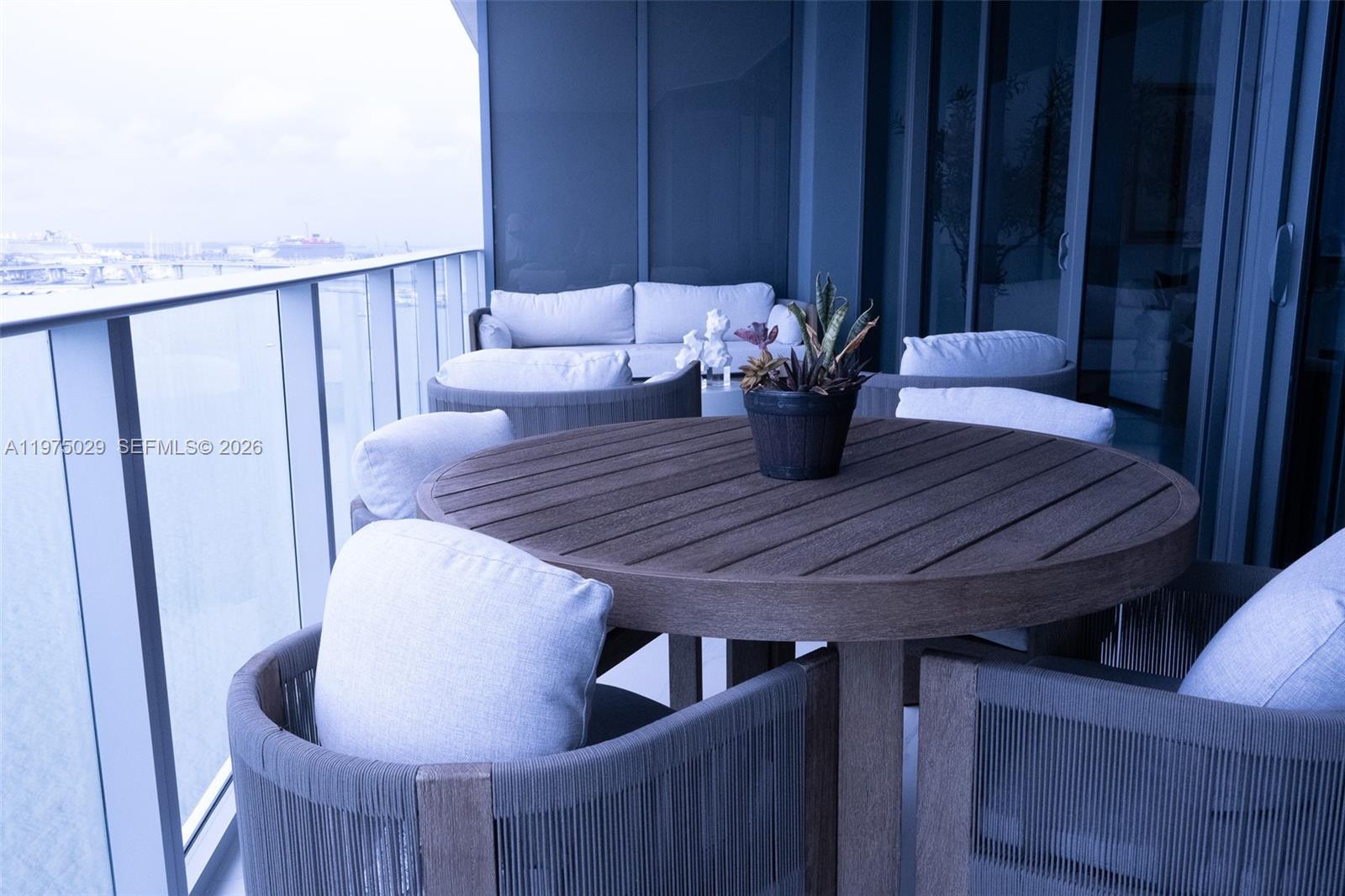 A balcony features a round wooden table with chairs and a sofa overlooking the water — 711 NE 23rd Ter # 1506, Miami FL 33137, MIAMI, FL