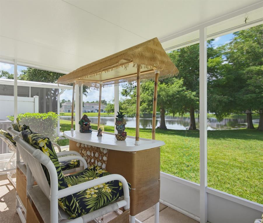 A screened-in patio features a tiki bar and chairs overlooking a grassy yard and pond — 2690 SICILY DRIVE, NEW SMYRNA BEACH, FL