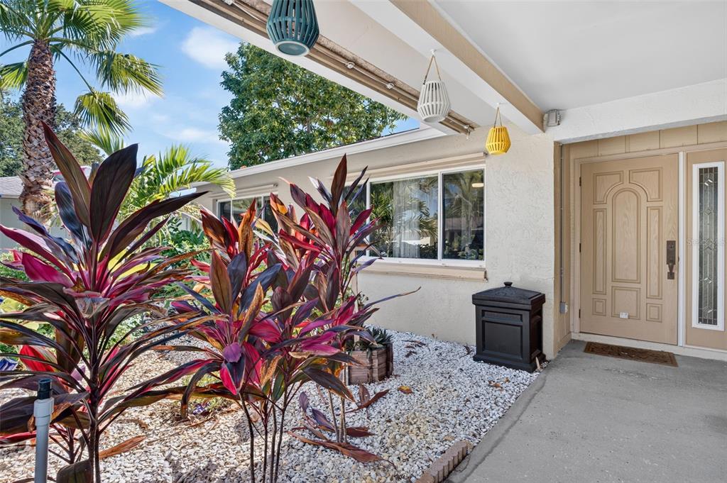 A front porch features a beige door, hanging lanterns, and a garden with colorful plants — 9259 119TH WAY, SEMINOLE, FL