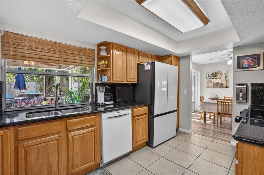 A kitchen with wood cabinets, black countertops, white appliances, and a view of the patio — 9259 119TH WAY, SEMINOLE, FL