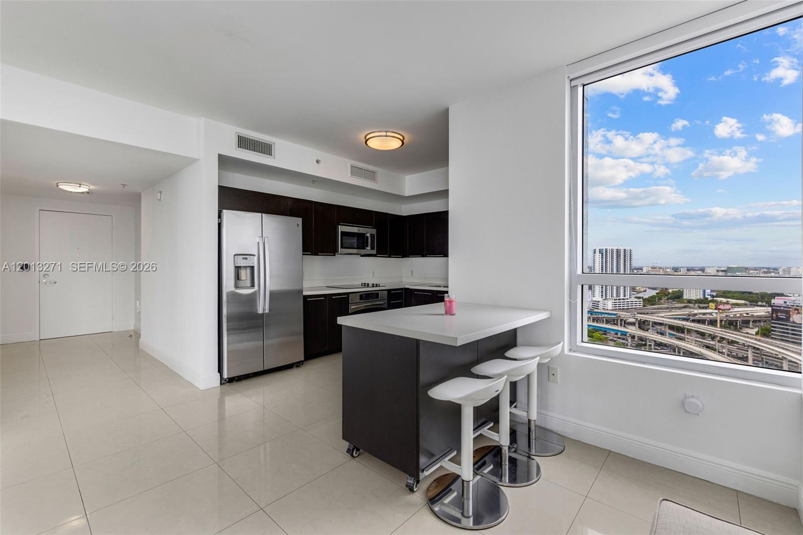 A modern kitchen features dark cabinetry, stainless steel appliances, a rolling island, and city views — 90 SW 3rd St # 2504, Miami FL 33130, MIAMI, FL