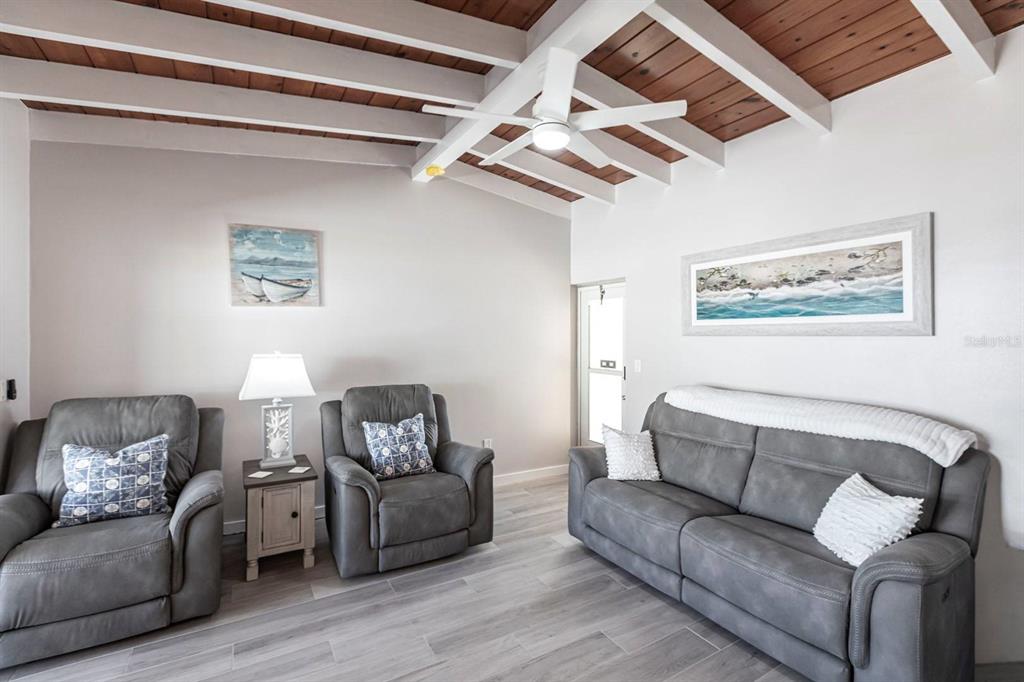 A living room features gray reclining furniture, a wood-plank ceiling, and light-colored tile flooring — 6006 MIDNIGHT PASS ROAD UNIT 65, SARASOTA, FL