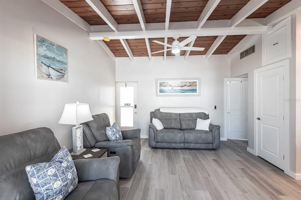 A living room features gray furniture, wood-plank flooring, and a white exposed-beam ceiling — 6006 MIDNIGHT PASS ROAD UNIT 65, SARASOTA, FL