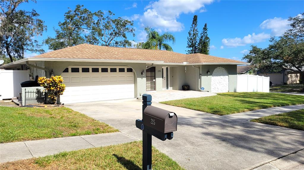 A single-story house with a white garage door, a paved driveway, and a brown roof — 215 MEADOWCROSS DRIVE, SAFETY HARBOR, FL