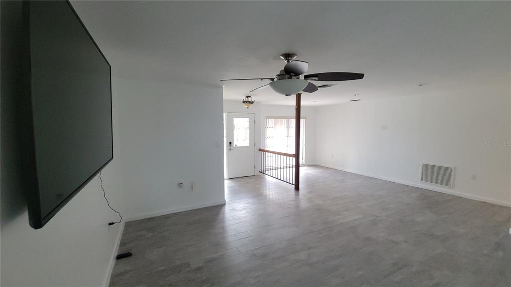 An empty living room features white walls, gray tile flooring, a ceiling fan, and a television — 215 MEADOWCROSS DRIVE, SAFETY HARBOR, FL