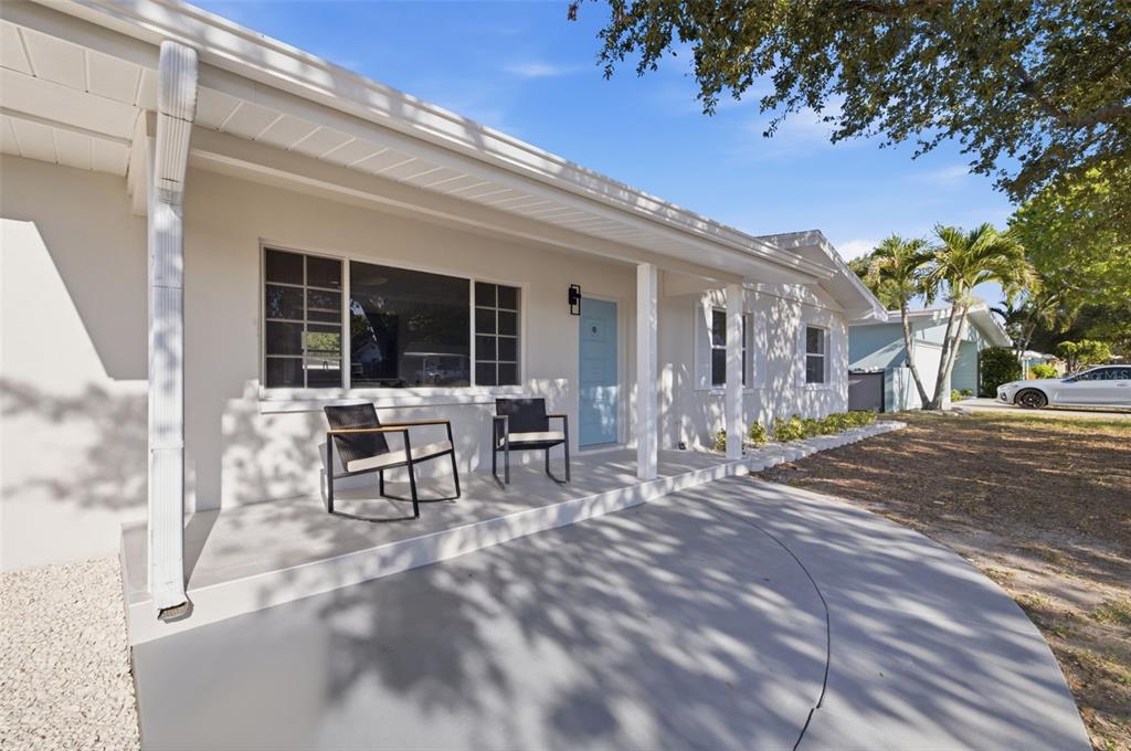 A light-colored house exterior features a covered front porch with two chairs and a door — 165 PINEWOOD AVENUE, CLEARWATER, FL
