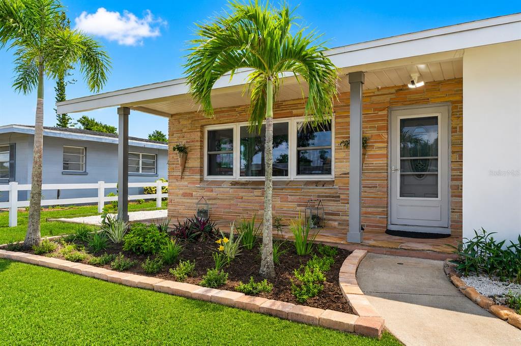 A house exterior features a stone facade, a covered porch, palm trees, and a white fence — 2711 27TH AVENUE DRIVE W, BRADENTON, FL