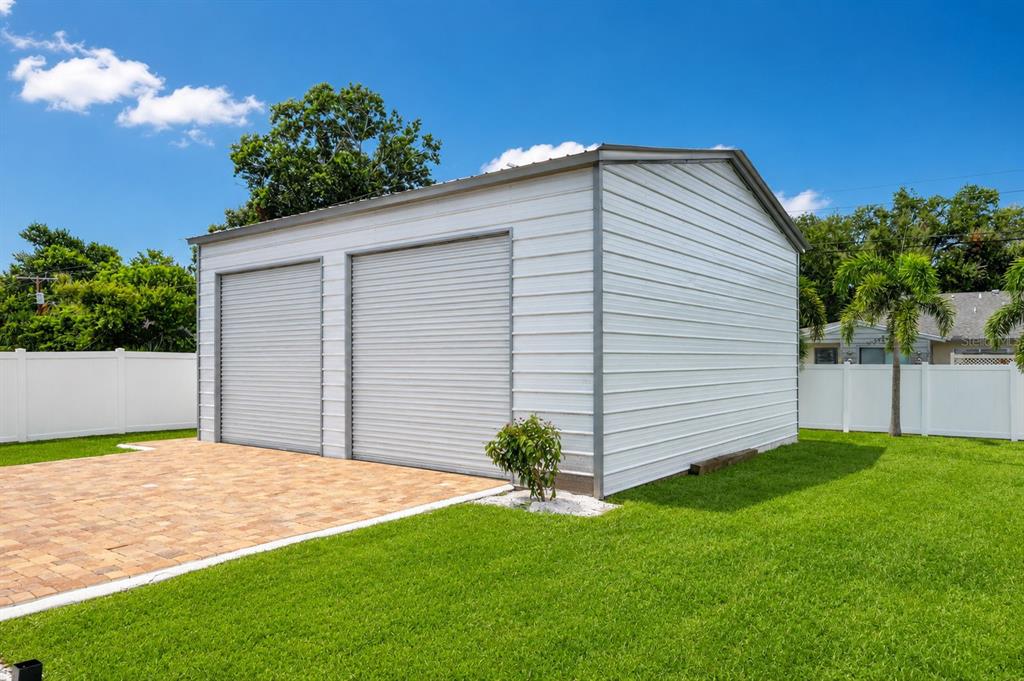 A white metal two-car garage sits on a paved patio in a grassy backyard — 2711 27TH AVENUE DRIVE W, BRADENTON, FL