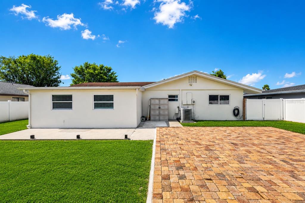 The exterior of a single-story house features a paved patio, green lawn, and white fencing — 2711 27TH AVENUE DRIVE W, BRADENTON, FL