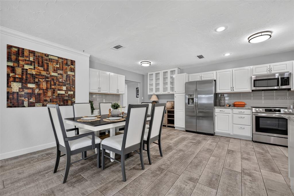 A dining area with a table and chairs next to a kitchen with white cabinets — 2711 27TH AVENUE DRIVE W, BRADENTON, FL