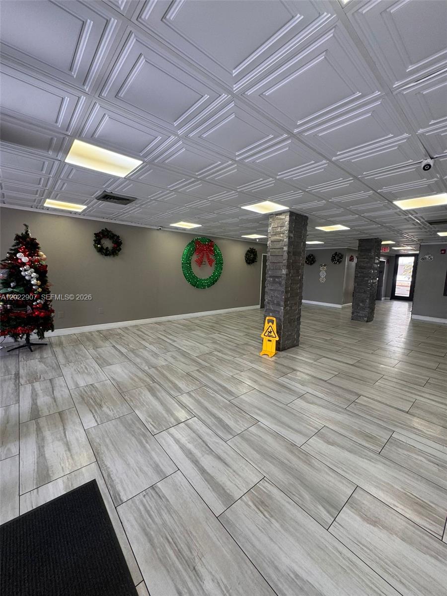 A spacious room features light wood-look tile flooring, a coffered ceiling, and stone-clad support columns — 15600 NW 7th Ave # 507, Miami FL 33169, MIAMI, FL