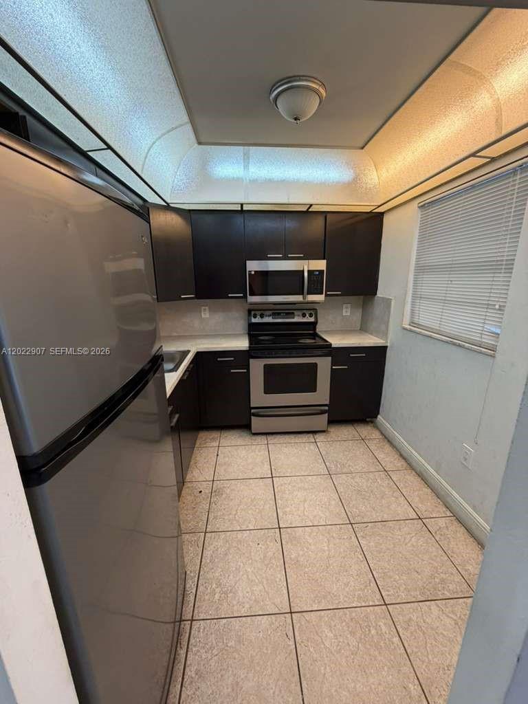 A galley kitchen features dark cabinets, stainless steel appliances, and light-colored tile flooring — 15600 NW 7th Ave # 507, Miami FL 33169, MIAMI, FL