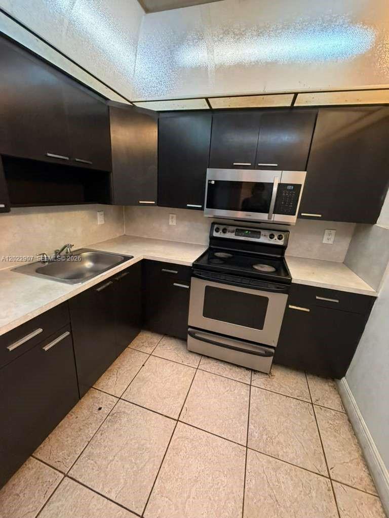 A kitchen features dark brown cabinets, stainless steel appliances, and light-colored countertops — 15600 NW 7th Ave # 507, Miami FL 33169, MIAMI, FL