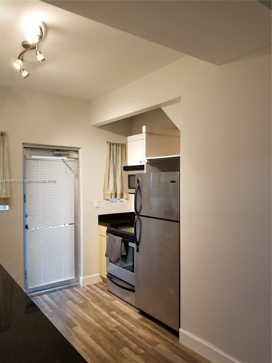 A kitchen features stainless steel appliances, light wood-look flooring, and a glass-paned exterior door — 1045 Meridian Ave # 5, Miami Beach FL 33139, MIAMI BEACH, FL