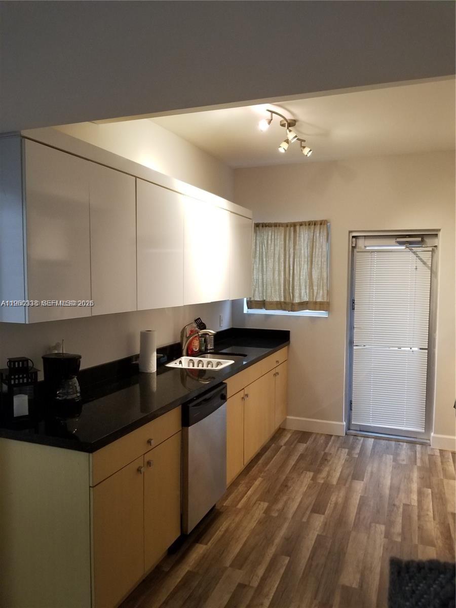 A kitchen features light wood lower cabinets, white upper cabinets, black countertops, and wood-look flooring — 1045 Meridian Ave # 5, Miami Beach FL 33139, MIAMI BEACH, FL