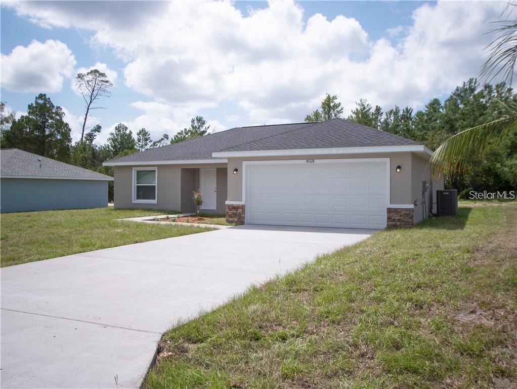 A single-story house with a beige stucco exterior, a two-car garage, and a concrete driveway — 17399 SW 25TH CIRCLE, OCALA, FL