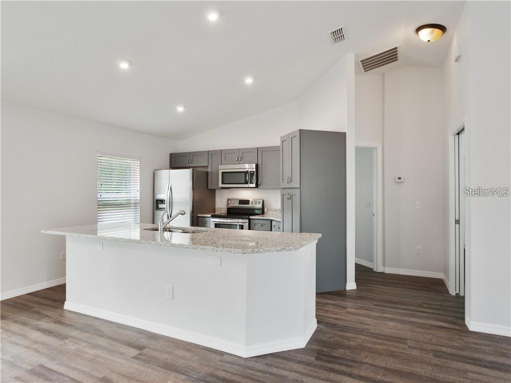 A kitchen features gray cabinets, granite countertops, a center island, and dark wood-look flooring — 17399 SW 25TH CIRCLE, OCALA, FL