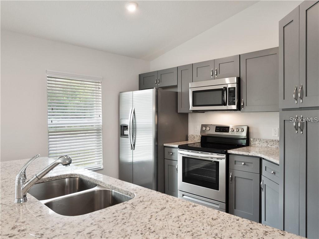 A kitchen features gray cabinets, stainless steel appliances, and a granite-topped island with a sink — 17399 SW 25TH CIRCLE, OCALA, FL