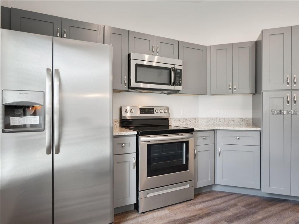 A kitchen features stainless steel appliances, gray cabinets, and speckled granite countertops — 17399 SW 25TH CIRCLE, OCALA, FL