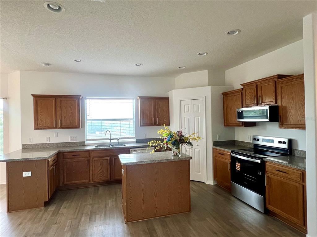 A kitchen features wood cabinets, granite countertops, a center island, and stainless steel appliances — 2234 N NORMANDY BOULEVARD, DELTONA, FL