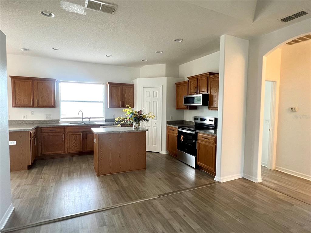A kitchen features wood cabinets, a center island, stainless steel appliances, and light wood flooring — 2234 N NORMANDY BOULEVARD, DELTONA, FL