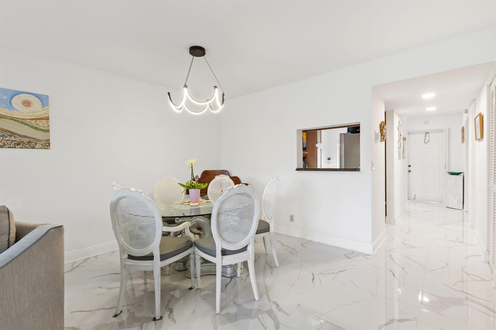 A dining area features a glass table, white cane-back chairs, and white marble-look flooring — 10110 Cedar Point Boulevard # 102, Boynton Beach FL 33437, BOYNTON BEACH, FL