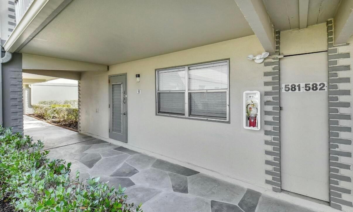 A covered outdoor walkway features a gray door, a window, and a wall-mounted fire extinguisher — 581 Monaco Boulevard # 581, Delray Beach FL 33446, DELRAY BEACH, FL