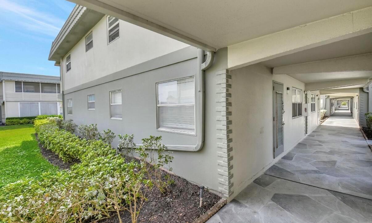 A gray apartment building exterior features a covered walkway, stone-patterned flooring, and landscaped bushes — 581 Monaco Boulevard # 581, Delray Beach FL 33446, DELRAY BEACH, FL