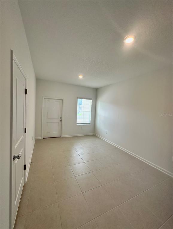 An empty room with light-colored tile flooring, white walls, a door, and a window — 6041 ZEN WAY, CLERMONT, FL