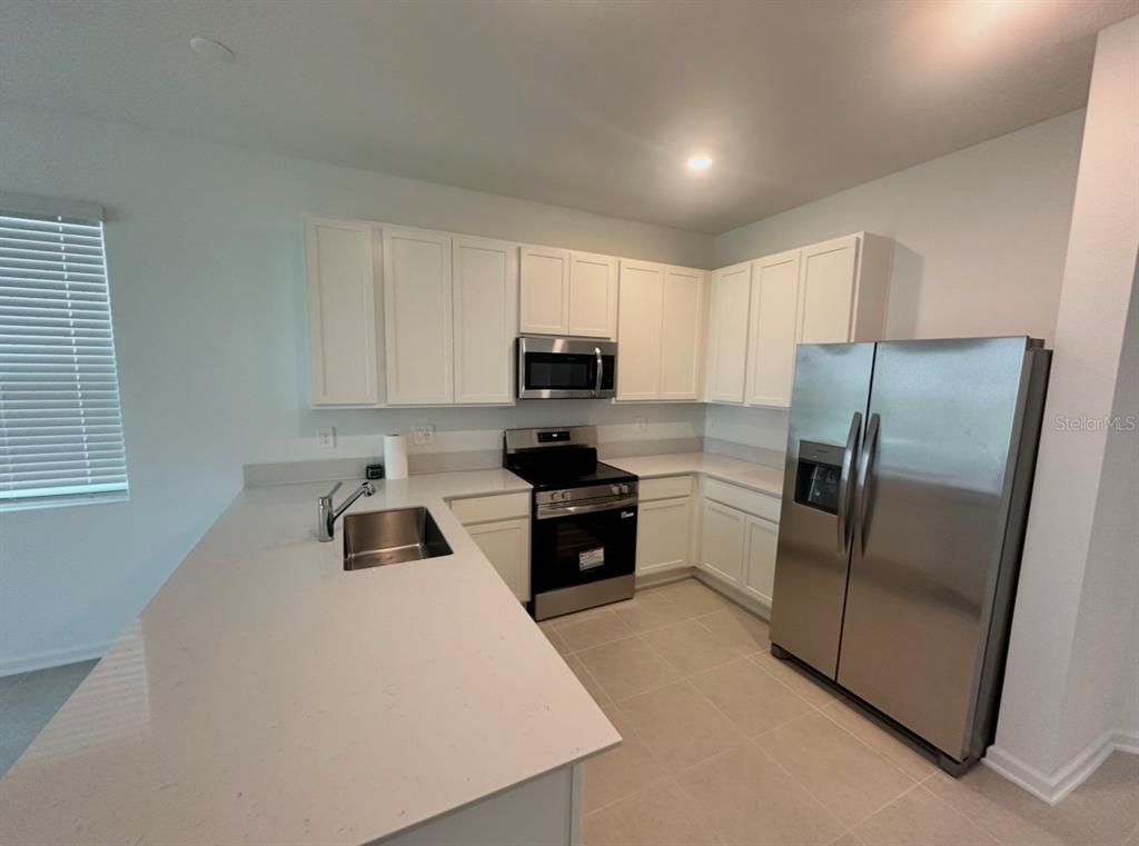 A kitchen features white cabinets, stainless steel appliances, and a light-colored quartz countertop island — 6041 ZEN WAY, CLERMONT, FL