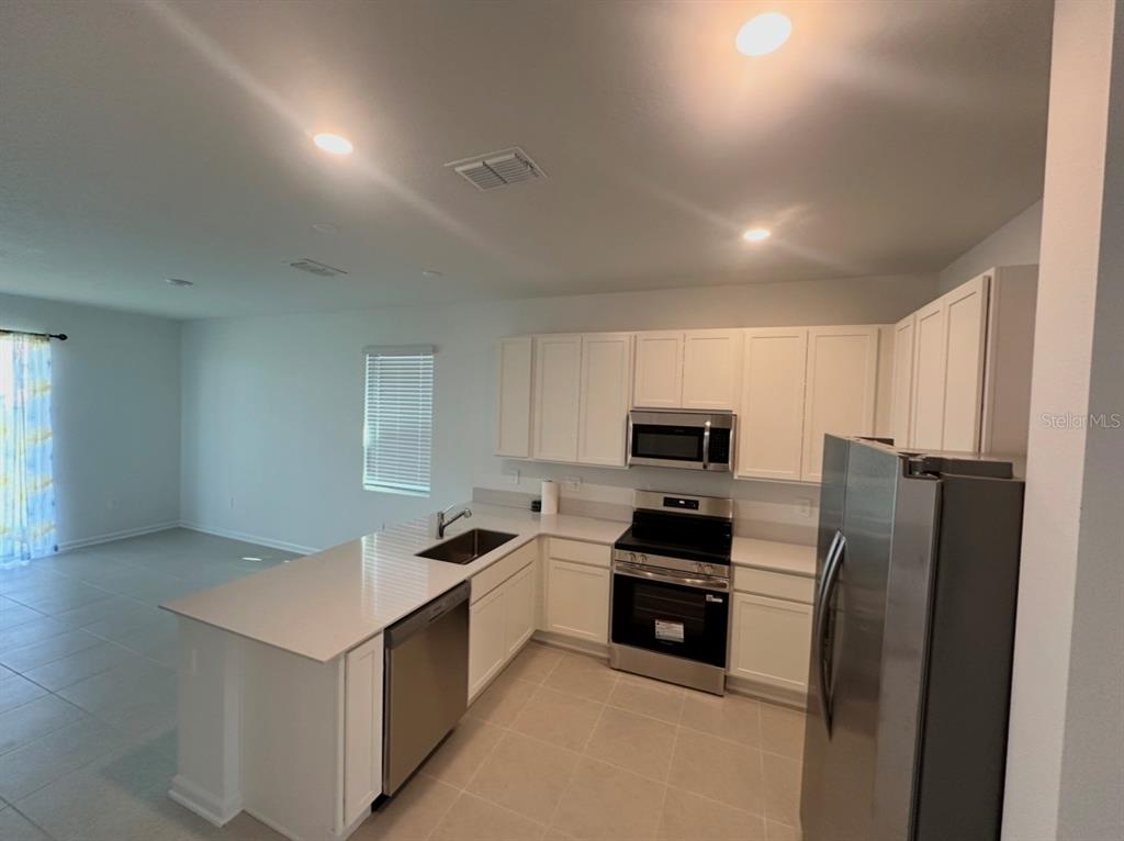 A kitchen with white cabinets, stainless steel appliances, and a peninsula island with a sink — 6041 ZEN WAY, CLERMONT, FL