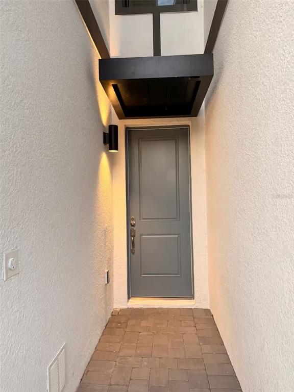 A gray front door is set in a narrow, stucco-walled entryway with brick pavers — 10437 EBB TIDE LANE, ORLANDO, FL