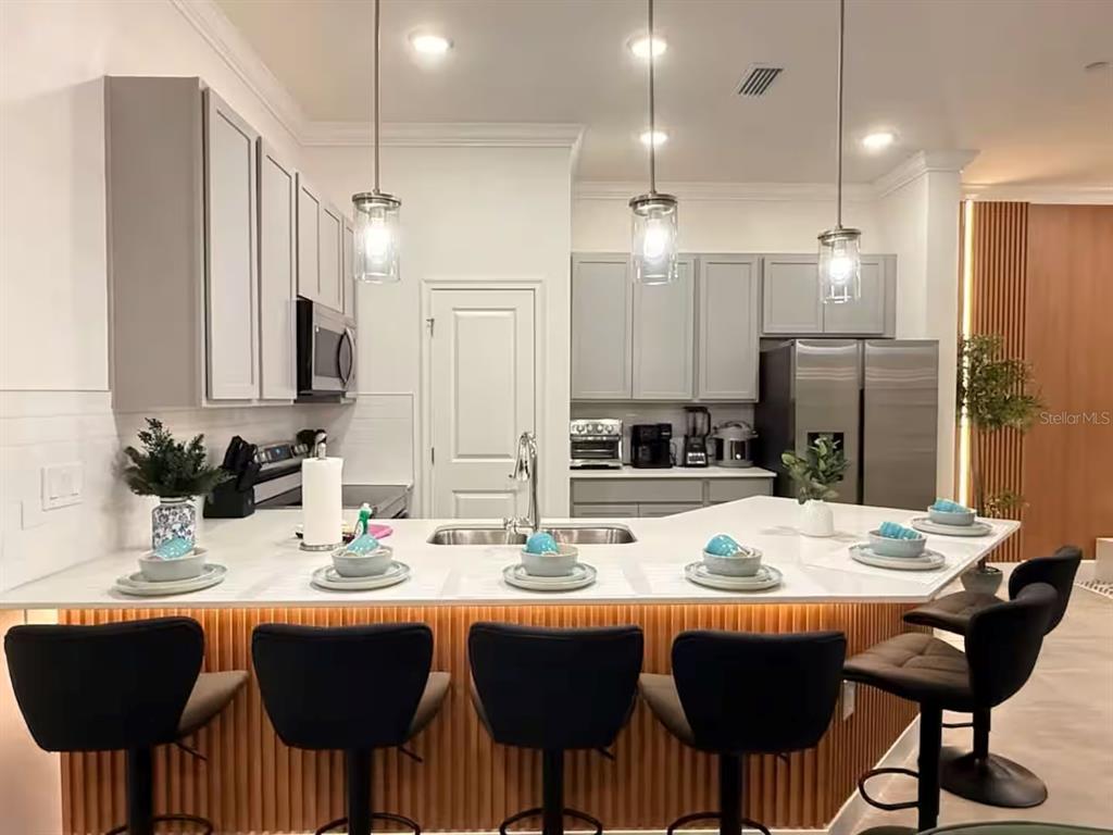 A kitchen features gray cabinets, white countertops, a slatted island base, and five bar stools — 10437 EBB TIDE LANE, ORLANDO, FL