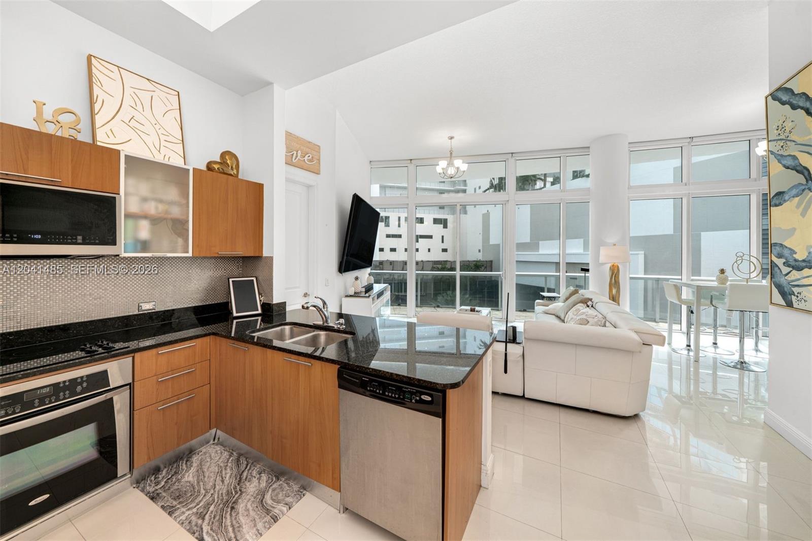 A modern kitchen with wood cabinets and granite countertops opens into a bright living area — 480 NE 30th St # 501, Miami FL 33137, MIAMI, FL