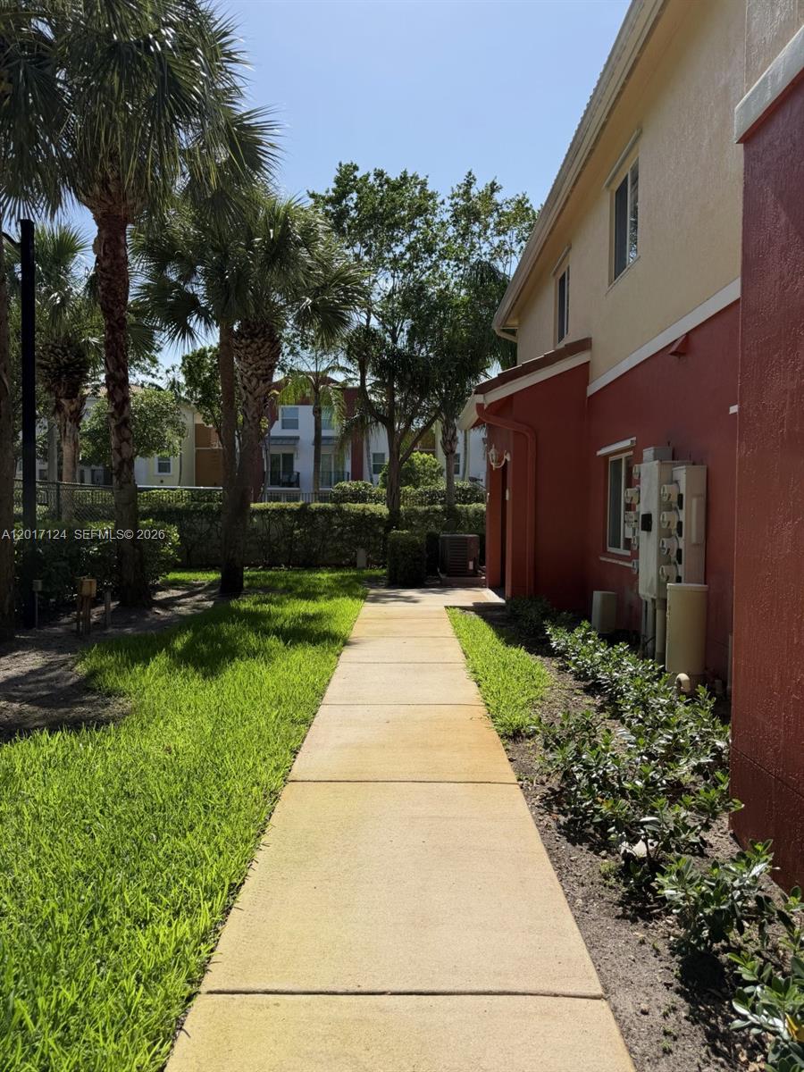 A concrete walkway leads along the side of a multi-story building with red exterior walls — 3335 Palomino Dr # 3, Davie FL 33024, DAVIE, FL