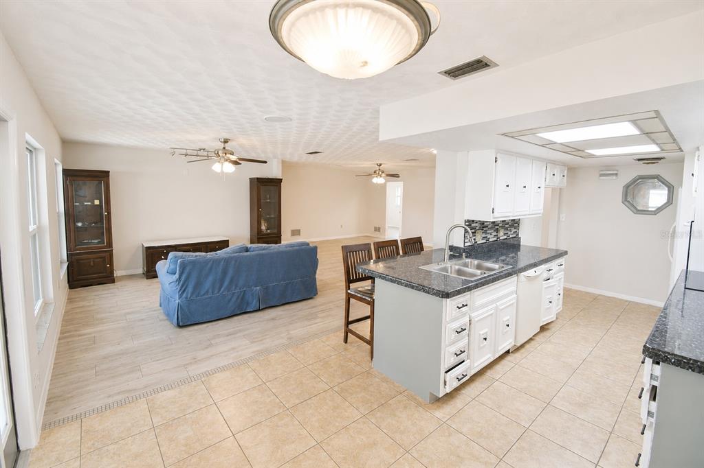 A kitchen with a gray island and white cabinets overlooks an open-concept living room area — 22128 BRONXVILLE AVENUE, PORT CHARLOTTE, FL