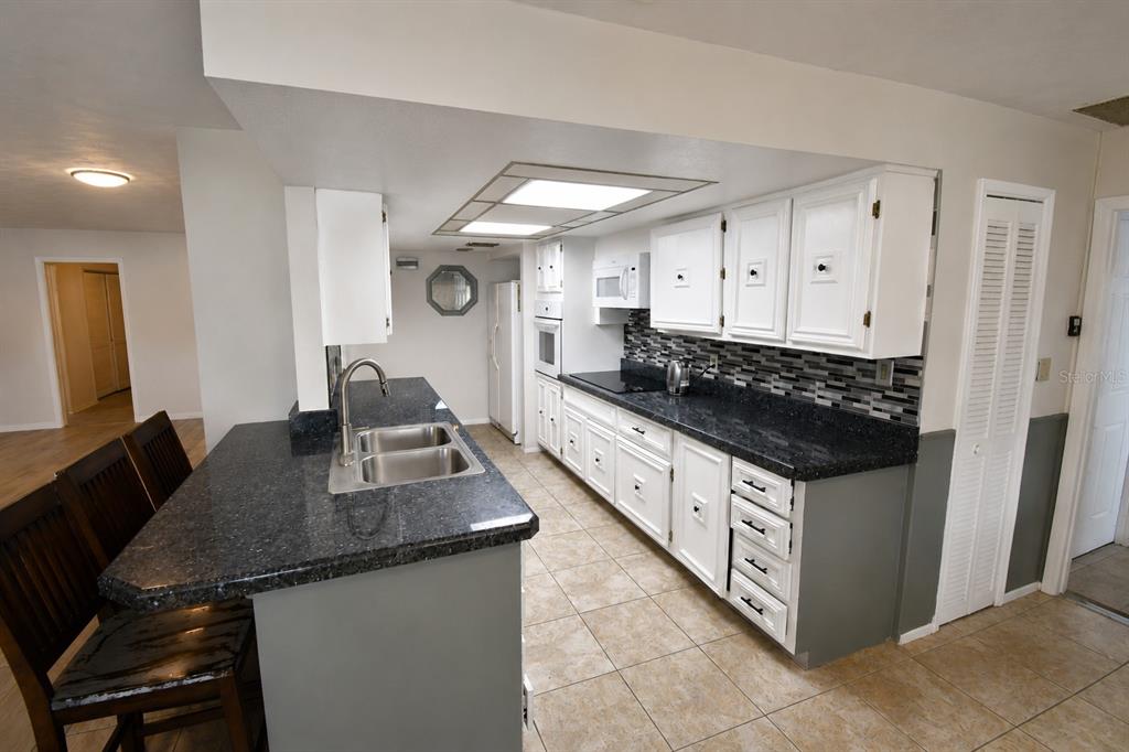 A kitchen features white cabinets, dark granite countertops, a tiled backsplash, and tile flooring — 22128 BRONXVILLE AVENUE, PORT CHARLOTTE, FL