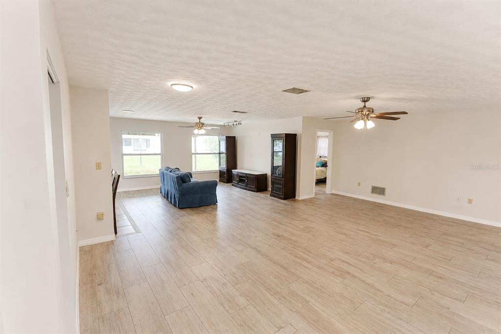 A spacious living room features light wood-look tile flooring, white walls, and two ceiling fans — 22128 BRONXVILLE AVENUE, PORT CHARLOTTE, FL