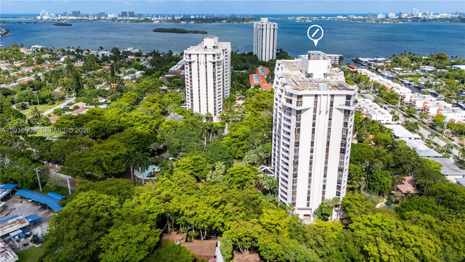 An aerial view shows two tall residential buildings surrounded by dense trees near a bay — 2000 Towerside Ter # 311, Miami FL 33138, MIAMI, FL