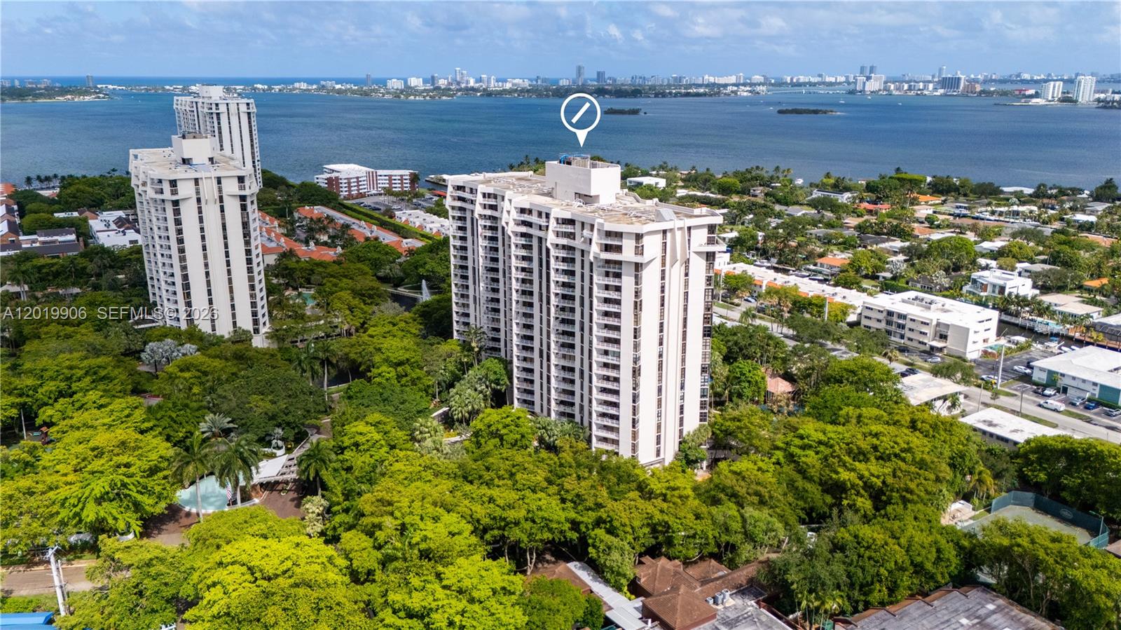 An aerial view shows two tall residential buildings surrounded by dense trees near a bay — 2000 Towerside Ter # 311, Miami FL 33138, MIAMI, FL