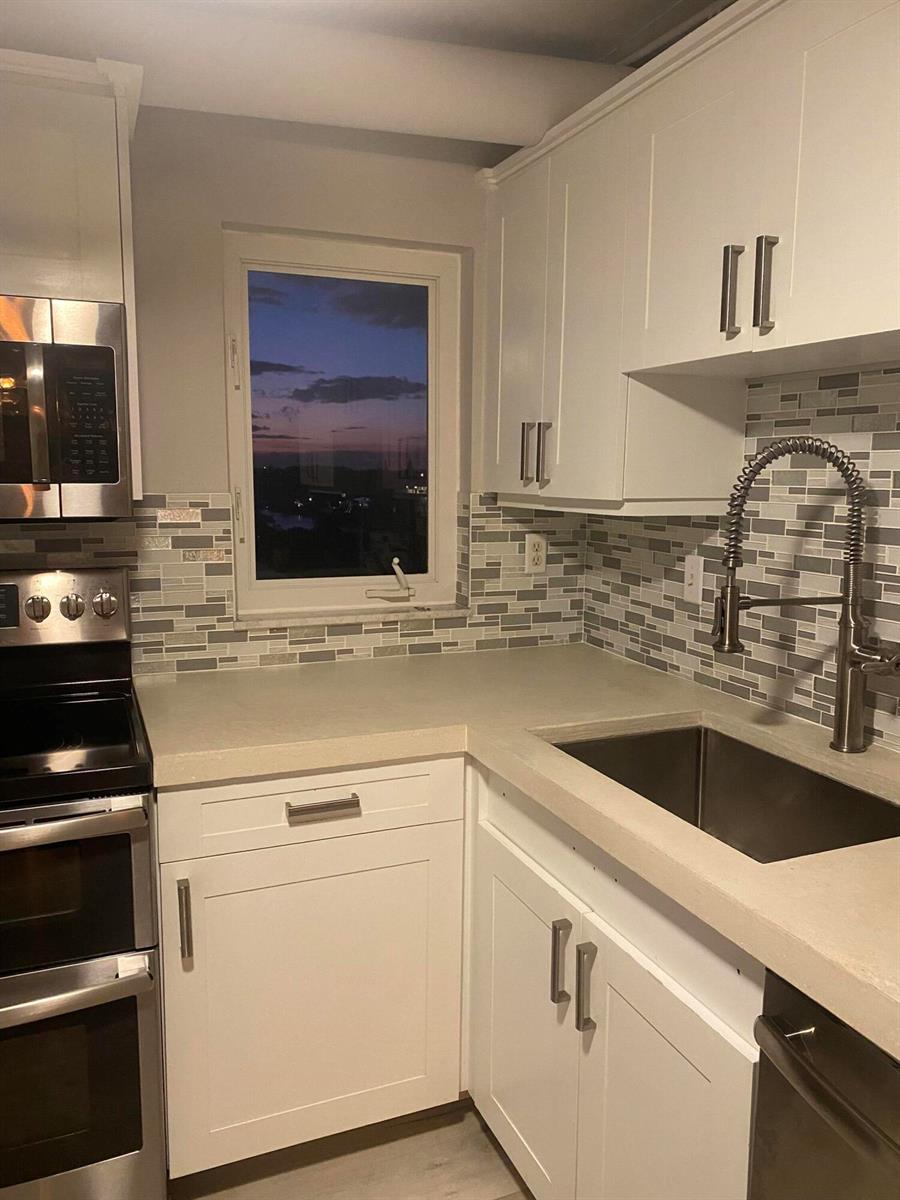 A kitchen features white cabinets, a light-colored countertop, a tiled backsplash, and a window view — 3215 S Ocean Boulevard # 402, Highland Beach FL 33487, HIGHLAND BEACH, FL
