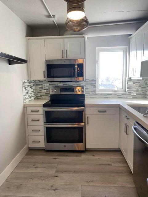 A kitchen features white cabinets, stainless steel appliances, a tiled backsplash, and wood-look flooring — 3215 S Ocean Boulevard # 402, Highland Beach FL 33487, HIGHLAND BEACH, FL