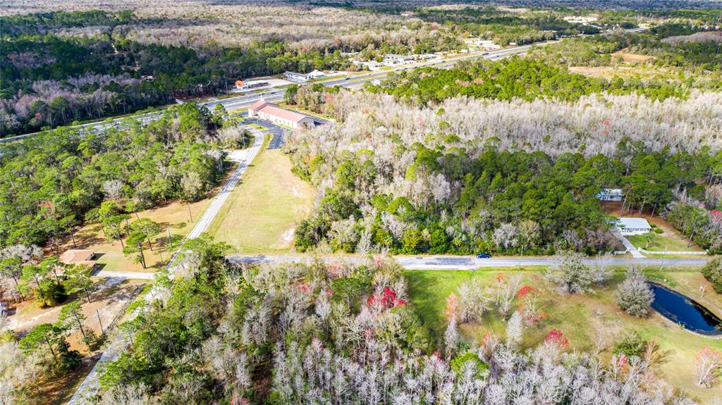 An aerial view shows a wooded lot with a road, a pond, and nearby buildings — 4925 S MORNINGSIDE TERRACE, HOMOSASSA, FL