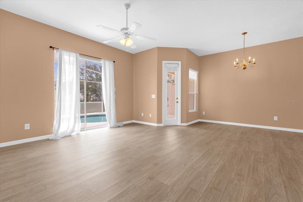 A spacious living room features light wood-look flooring, tan walls, a ceiling fan, and sliding doors — 516 BRUNELLO DRIVE, DAVENPORT, FL