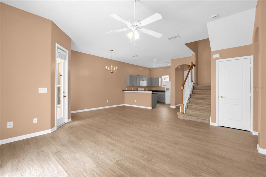 An open-concept living area features light wood-look flooring, tan walls, a kitchen, and carpeted stairs — 516 BRUNELLO DRIVE, DAVENPORT, FL